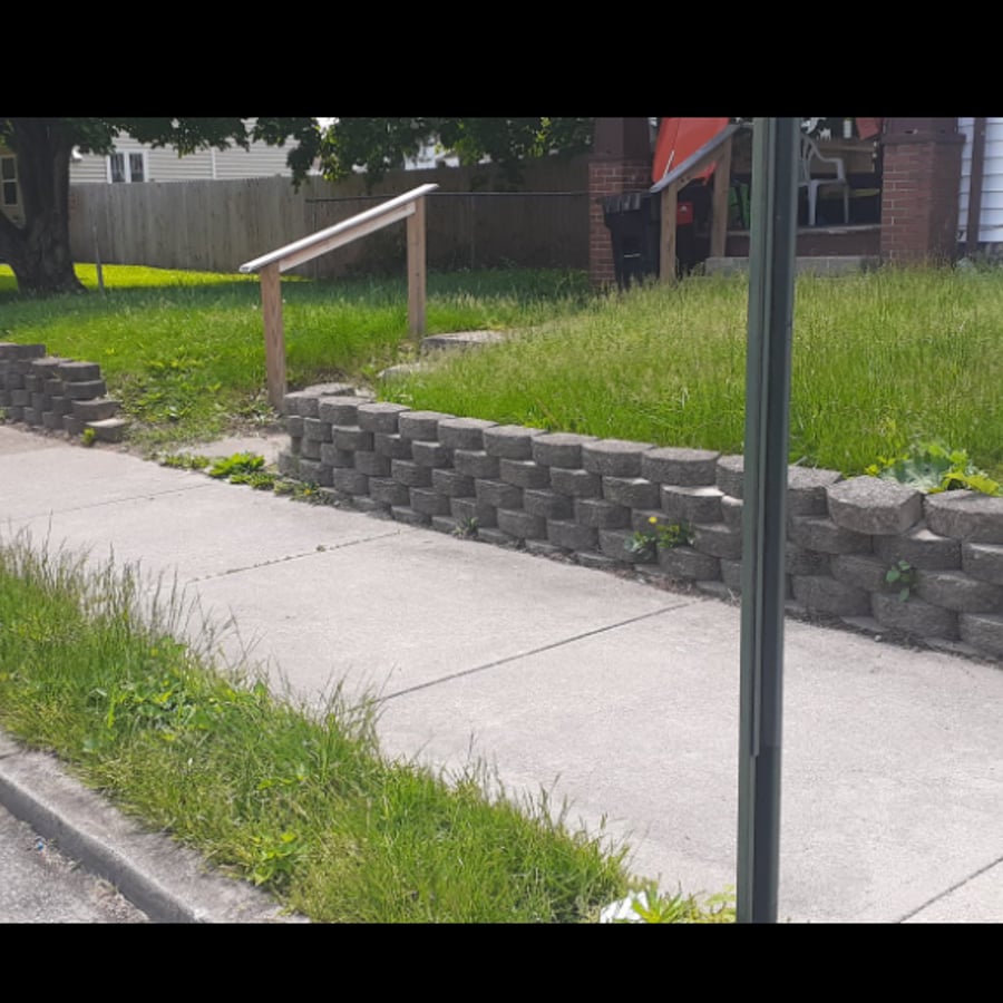 Before: overgrown lawn and weeds along retaining wall and sidewalk
